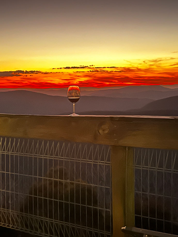 Glass of red wine on balcony railing in front of red sunset